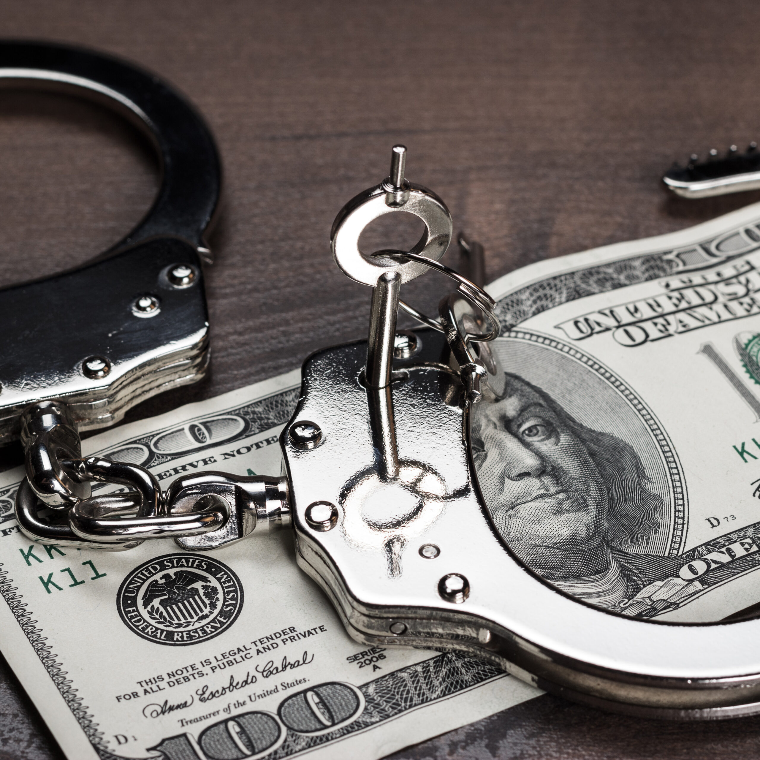 handcuffs with a key sitting on 100 dollar bill
